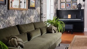 A living room with a green sofa, a black piano, and a geometric chandelier. - Kahili Suite - Historic charm meets Luxury (Wailuku)