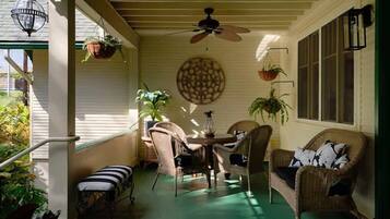 Un porche techado con mobiliario de mimbre, ventilador de techo y plantas colgantes.