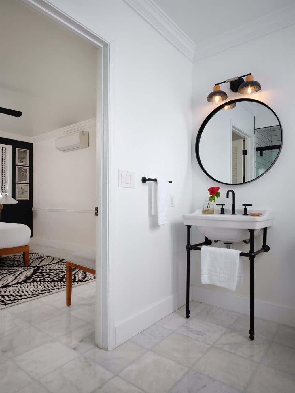 Une salle de bain avec un lavabo blanc, des tuyaux noirs, un miroir rond et un luminaire noir.