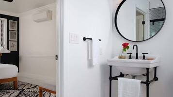 Une salle de bain avec un lavabo blanc, des tuyaux noirs, un miroir rond et un luminaire noir.