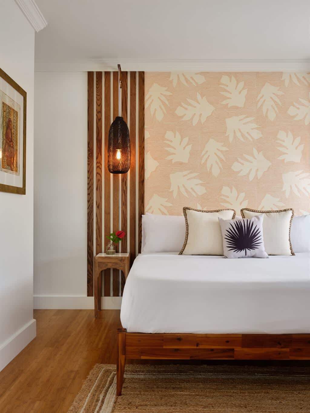 A bedroom with a wooden bed frame, a wall-mounted lamp, and a patterned wallpaper.