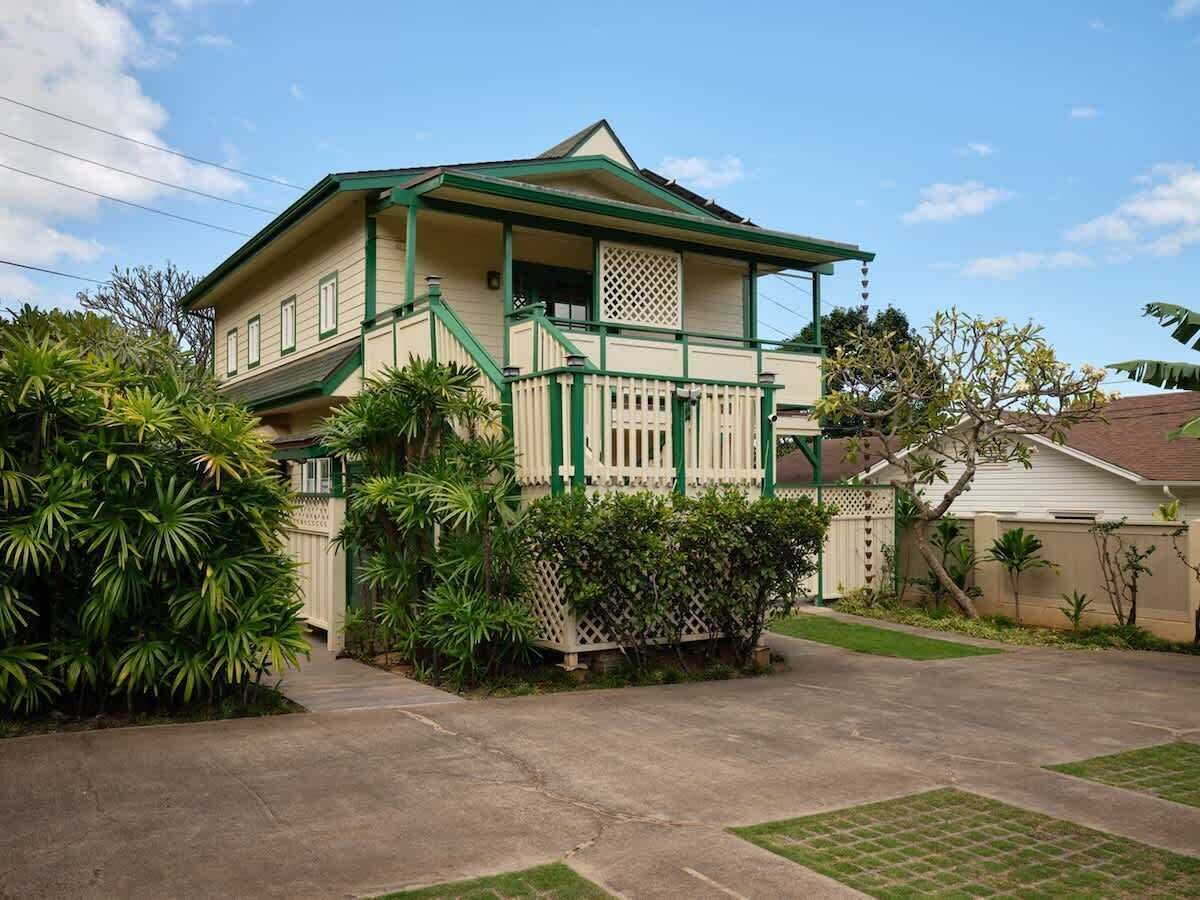 A two-story house with a green roof, white exterior, and a front porch with a lattice railing.