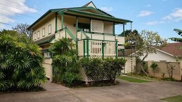 A two-story house with a green roof, white exterior, and a front porch with a lattice railing.