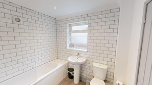 A bathroom with white subway tiles, a bathtub, a sink, a toilet, and a window with frosted glass.