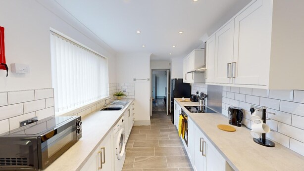 A modern kitchen with white cabinetry, a built-in oven, a dishwasher, and a coffee machine.