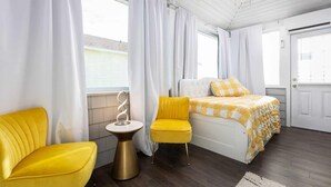 Un dormitorio moderno con una cama, dos sillas amarillas, una mesita redonda y una puerta blanca.