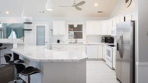 Una cocina moderna con armarios blancos, una isla de mármol con taburetes altos, un refrigerador de acero inoxidable y un ventilador de techo.