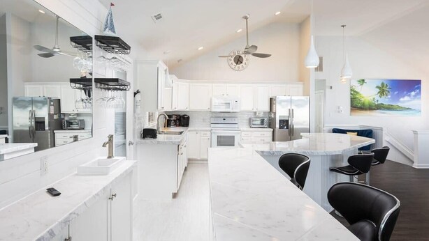 Una cocina moderna con armarios blancos, una isla central con taburetes de bar y una isla grande con microondas integrado.