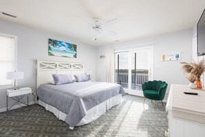 Une chambre à coucher avec un lit, une table de chevet, un fauteuil vert, un bureau et un balcon avec vue.