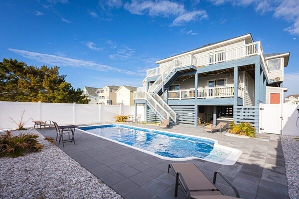 Une maison moderne à deux étages, dotée d’une piscine, d’un espace de détente extérieur et d’un escalier menant à un balcon.