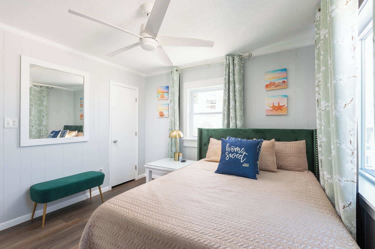 Une chambre à coucher comprenant un lit, un ventilateur de plafond, un banc, une table de chevet et une fenêtre avec des rideaux.