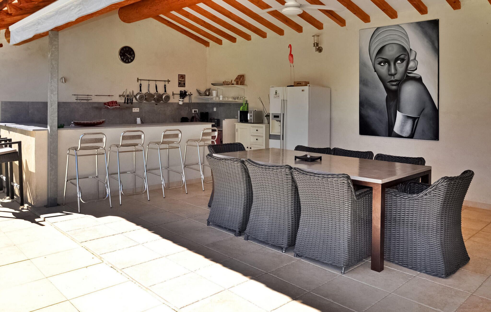Cocina moderna con comedor, que incluye una isla grande con taburetes de bar, una mesa de comedor con sillas de mimbre y una encimera con varios electrodomésticos.