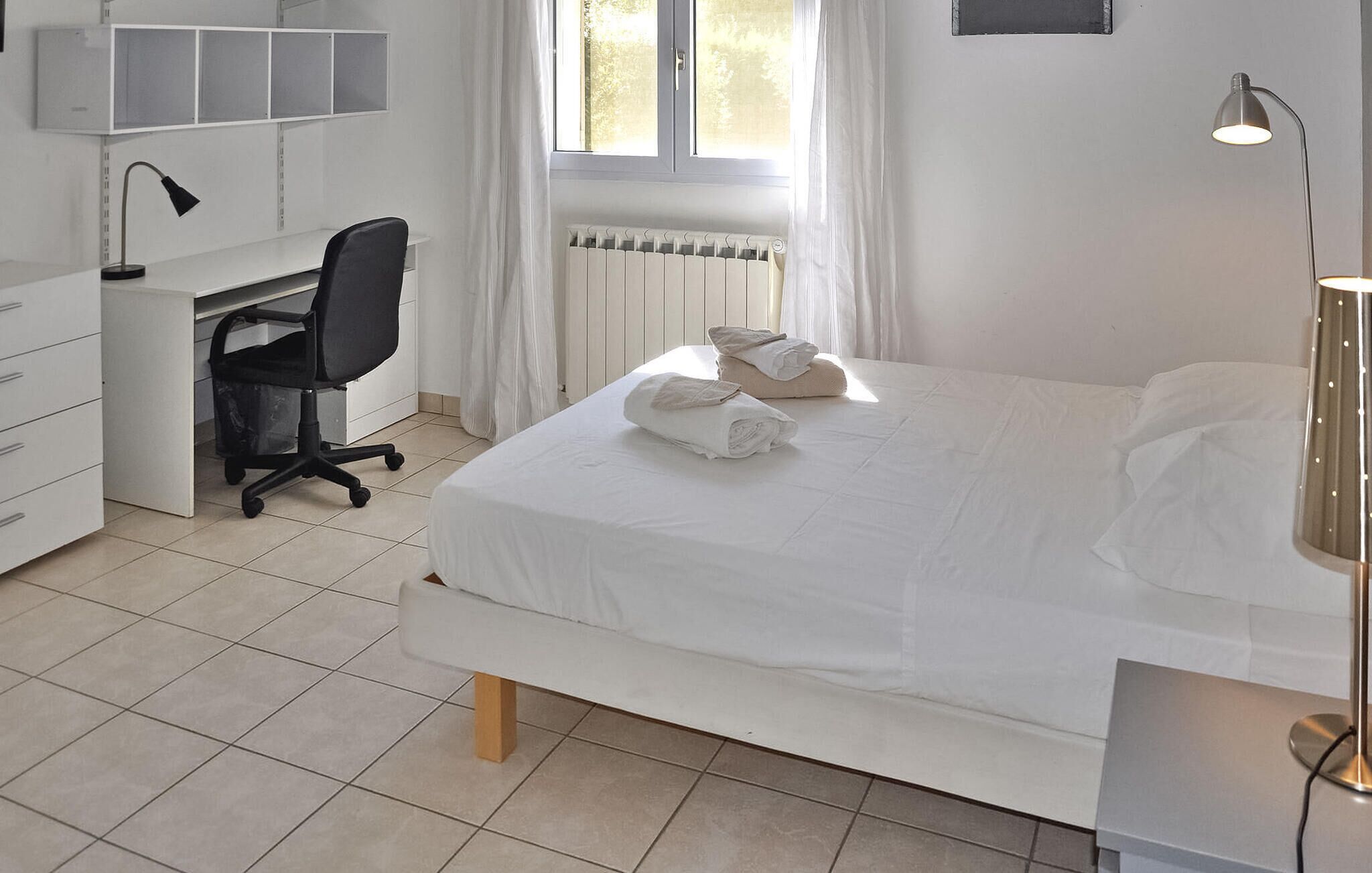 A hotel room with a bed, a desk, a chair, and a radiator.