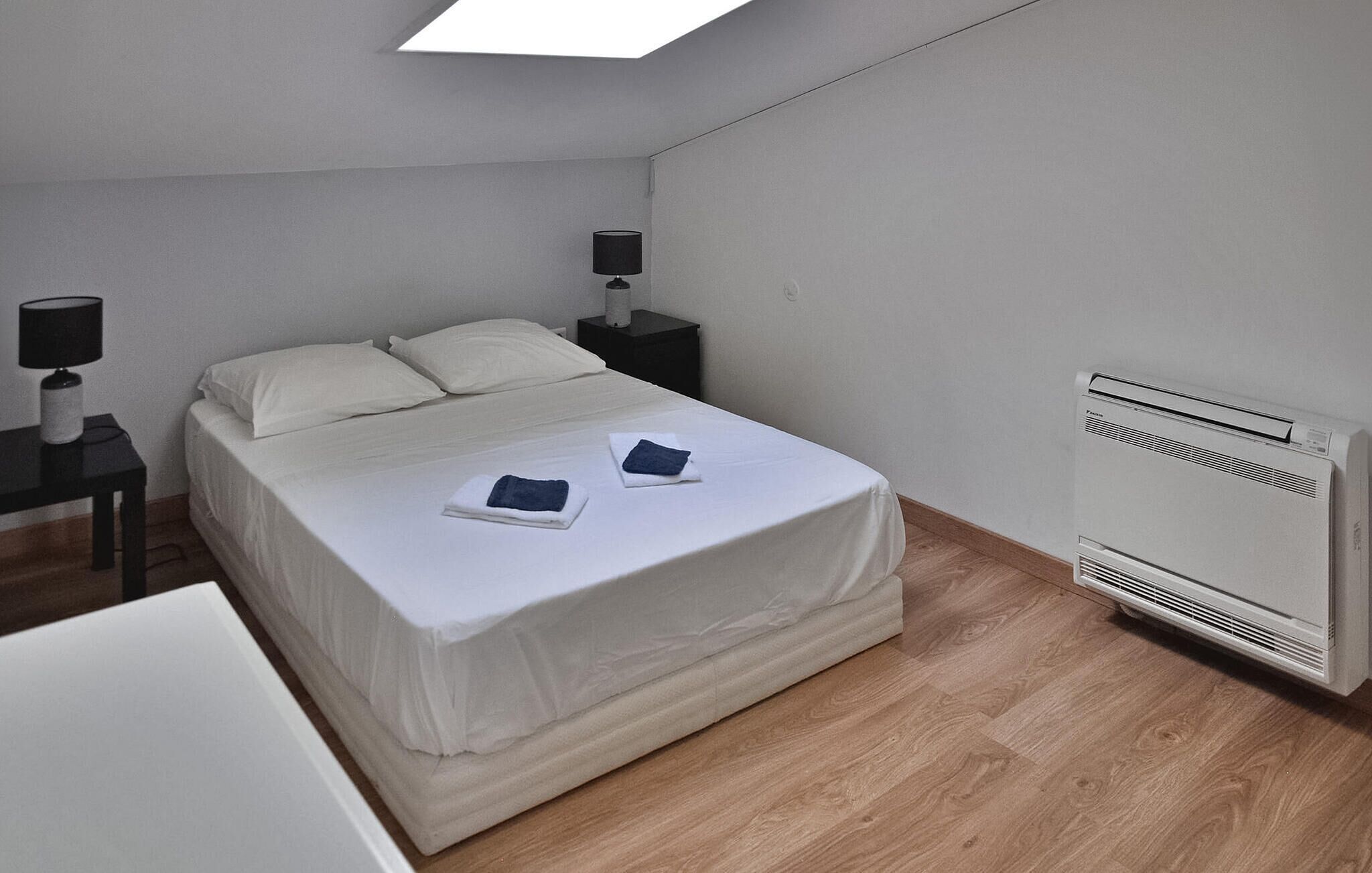 A bedroom with a bed, two bedside tables with lamps, a heater, and a wooden floor.