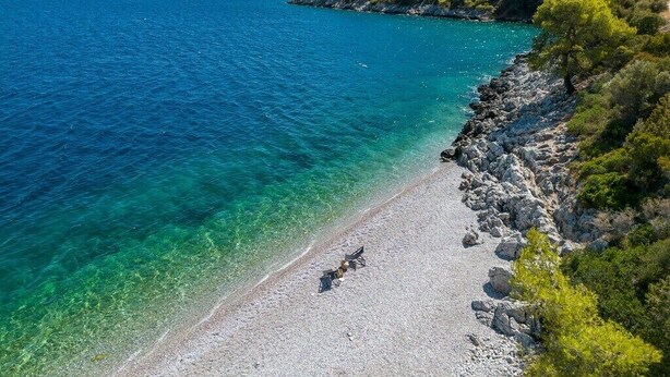Een strand met helder turquoise water, een rotsachtige kustlijn en weelderige groene begroeiing op een heuvel.