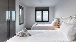 Een moderne hotelkamer met twee bedden, een groot raam met uitzicht, een plafondventilator en een glazen deur.