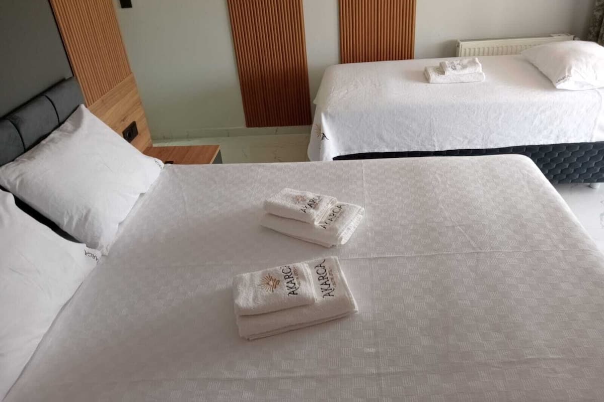 Habitación de hotel con dos camas, cada una con ropa blanca y una toalla doblada con la marca 'AKARCA'.