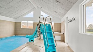 An indoor swimming pool with a blue slide and ladder, large windows, and a view of the outside. - Beautiful home in Idestrup with sauna (Idestrup)
