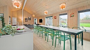 A modern kitchen with wooden walls, a long dining table with green chairs, and pendant lights. - Beautiful home in Idestrup with sauna (Idestrup)