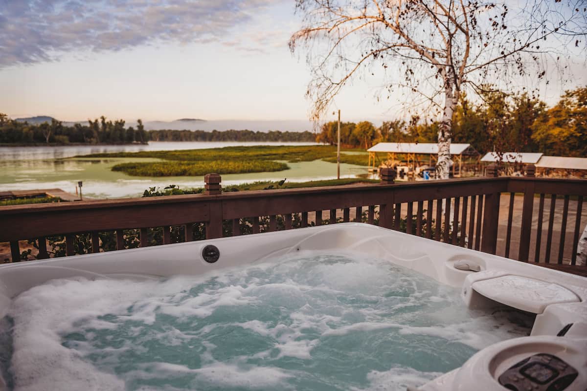 Banheira de hidromassagem com vista para um lago e árvores ao redor.