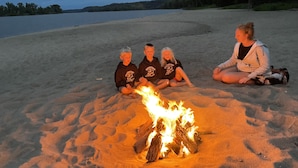 En gruppe mennesker sidder på en sandstrand med et bål i midten.