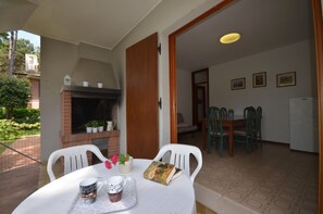 A patio with a table set for two, a brick fireplace, and a dining area with chairs and a table. - Lovely first floor villa with common garden (Bibione)