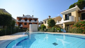 A swimming pool surrounded by modern buildings with balconies, a clear sky, and some greenery. - Adorable flat with common pool in Bibione (Bibione Pineda)
