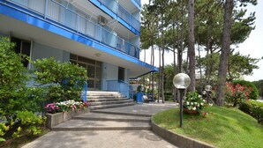 Un edificio de varios pisos con balcones azules, un camino de concreto que lleva a la entrada y zonas verdes alrededor.