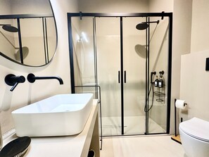 A modern bathroom with a large white sink, a glass-enclosed shower, and a toilet.