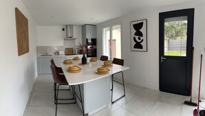 A modern kitchen with a white island, brown chairs, and a black door. - Maison d Isaure (Bergerac)