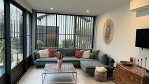 A modern living room with a sectional sofa, a coffee table, a wooden dresser, and a large window offering a view of the outdoors. - Maison d Isaure (Bergerac)