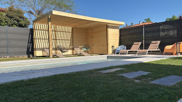 Un patio trasero con piscina, un pérgola de madera y sillas de descanso.