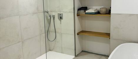 Un baño moderno con ducha de vidrio, bañera independiente y estantes empotrados con toallas.
