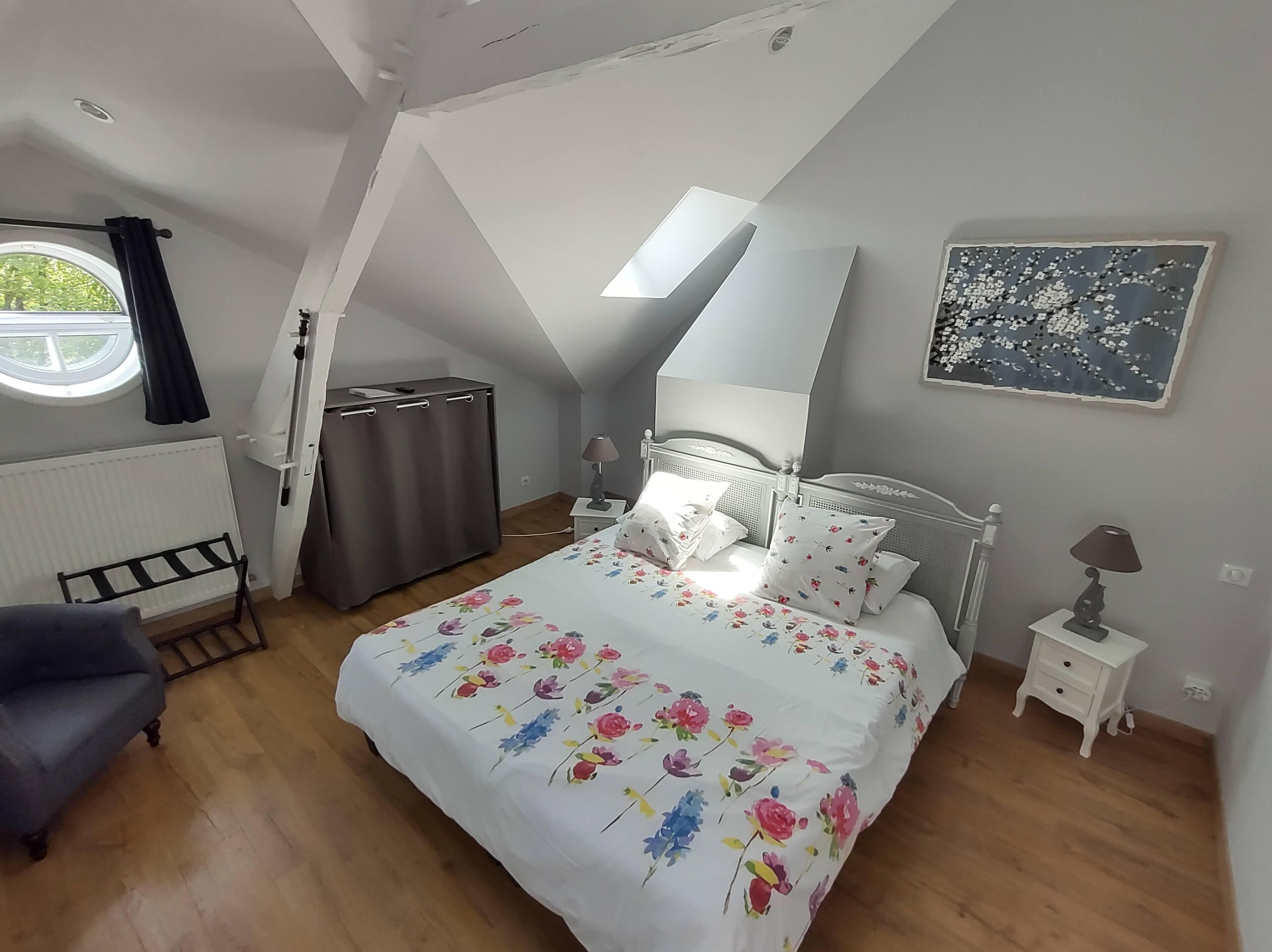 Un dormitorio con cama, mesita de noche, lámpara, radiador, silla y ventana con cortinas.