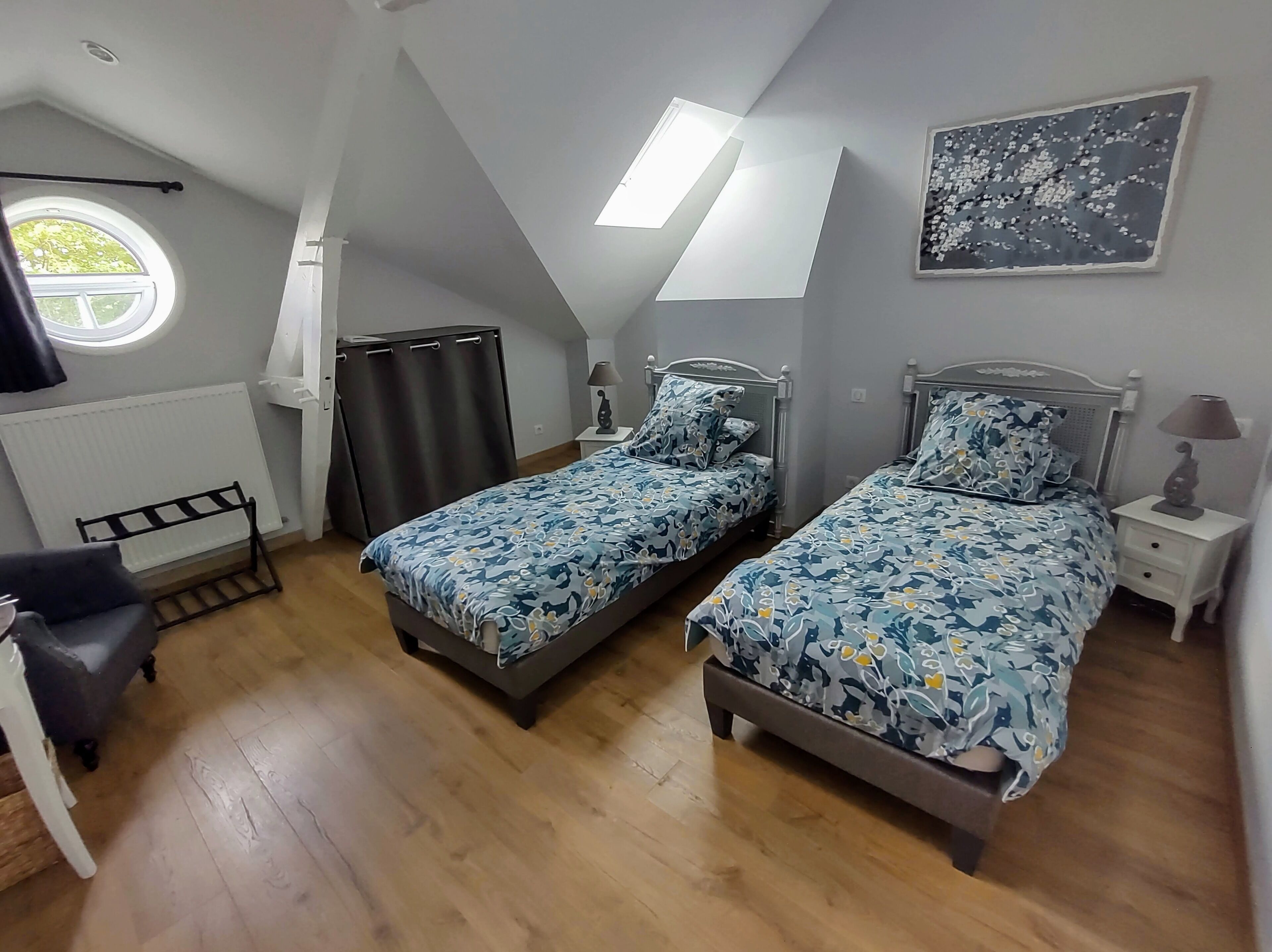 Une chambre avec deux lits, une fenêtre, un radiateur, une chaise et un tableau accroché au mur.