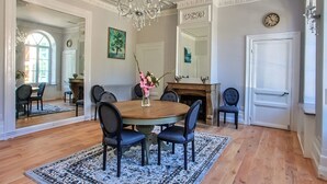 Een eetzaal met een ronde tafel, stoelen, een kroonluchter en een open haard.