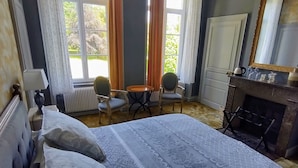 Een slaapkamer met een bed, een stoel, een dressoir, een spiegel en een open haard.