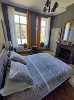 Um quarto com cama, poltrona, cômoda, espelho e lareira.