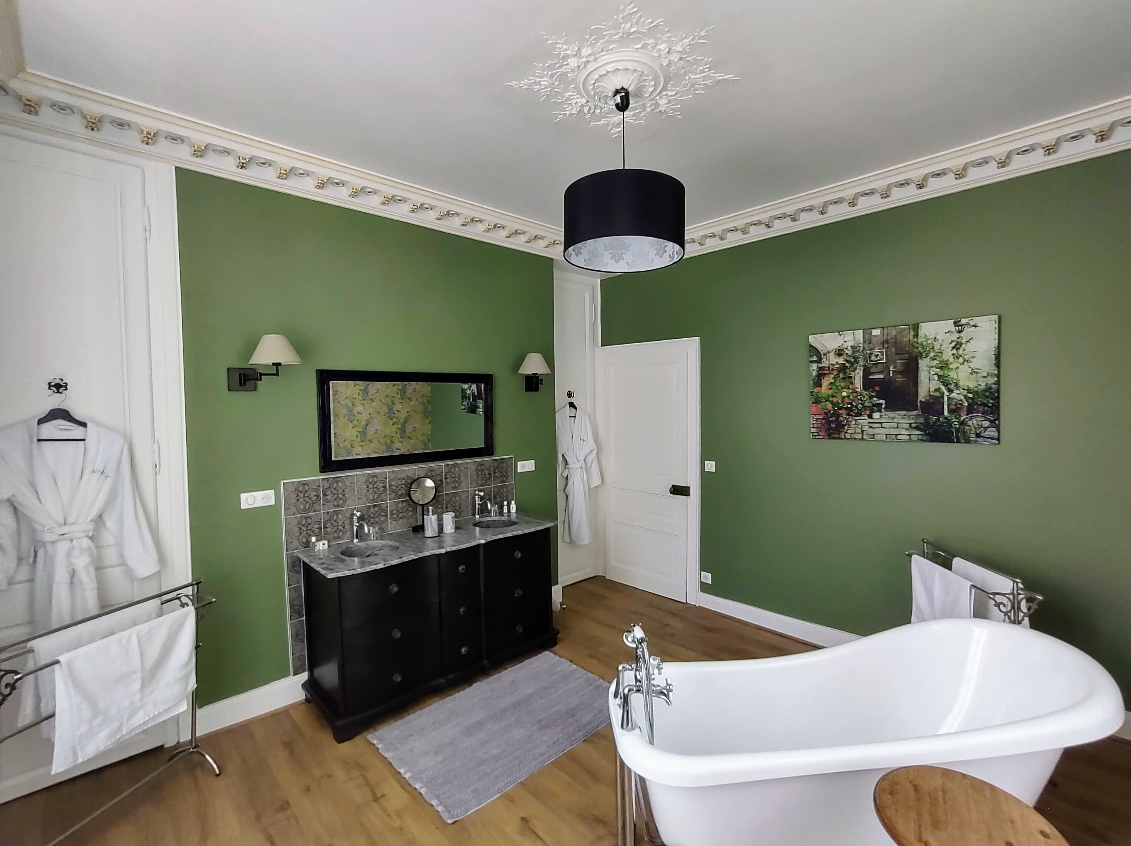A bathroom with green walls, a white bathtub, a double sink vanity, and a mirror.