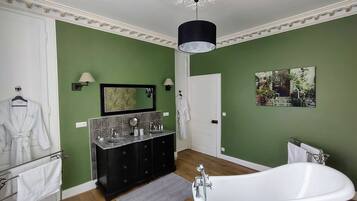 A bathroom with green walls, a white bathtub, a double sink vanity, and a mirror.