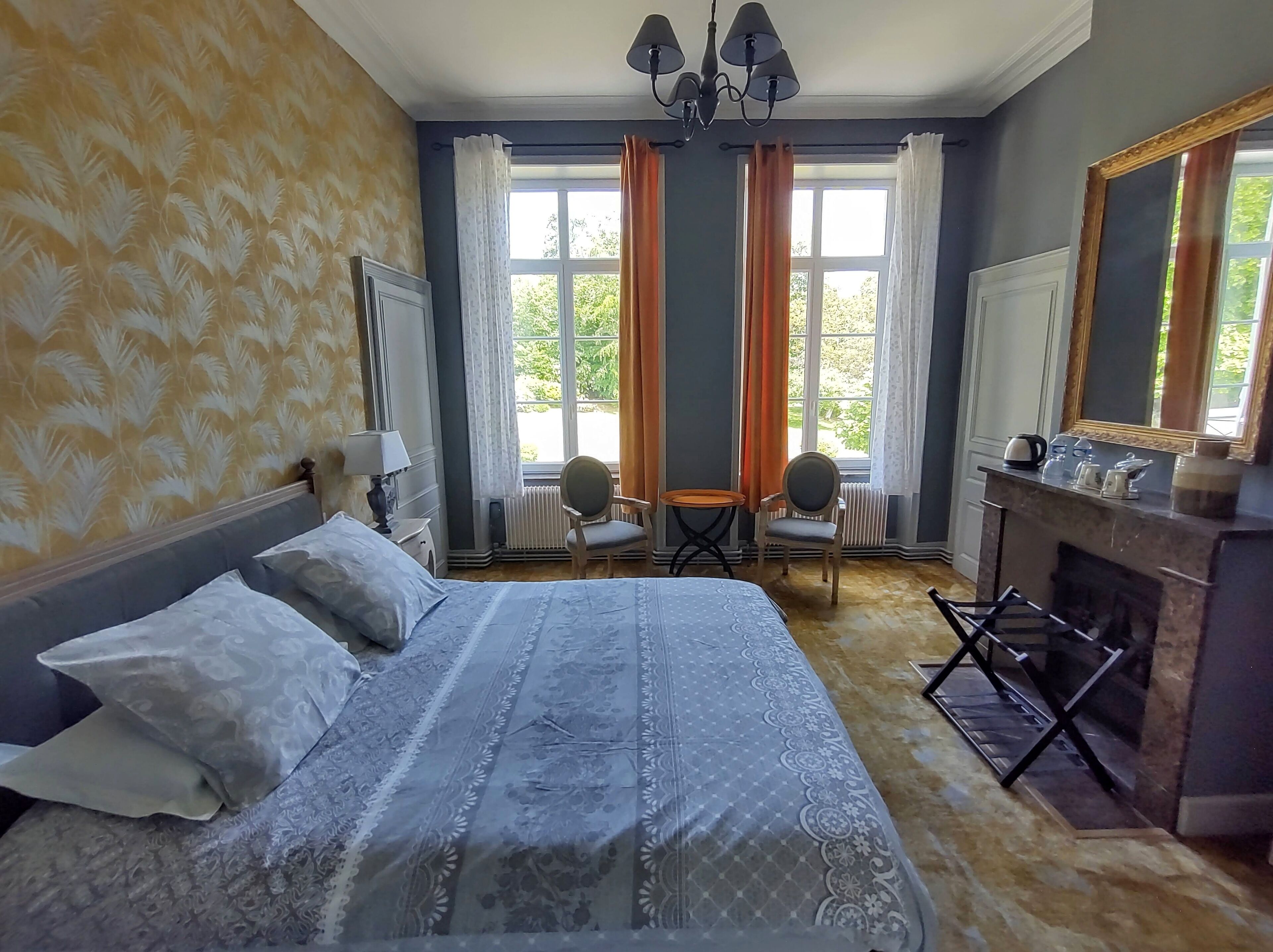Une chambre à coucher avec un grand lit, deux fauteuils, une cheminée et une fenêtre avec des rideaux.