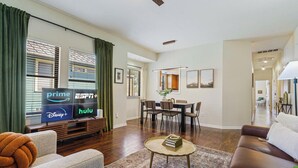 A modern living room with a flat-screen TV displaying streaming services, a dining area with a table and chairs, and a cozy seating area with a sofa and a coffee table. - Modern Haven with King Suite + Impeccable Location (Austin)