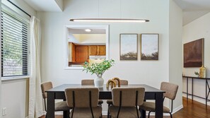 Un comedor con una mesa negra, cuatro sillas, un florero con flores y vistas a la cocina a través de una ventana.