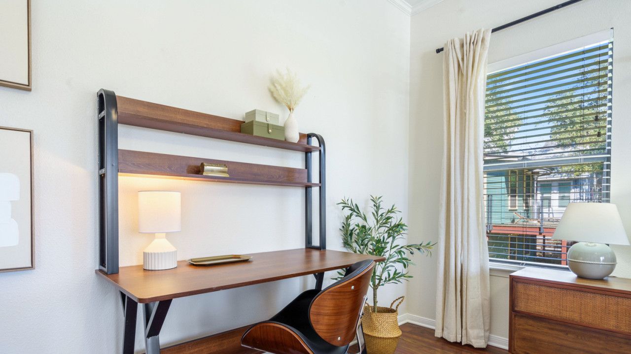 Un espace de bureau moderne comprenant un bureau en bois, une chaise, une lampe, une plante en pot et une fenêtre avec des stores.