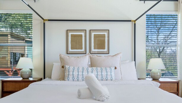 A hotel room with a large bed, two framed pictures on the wall, and a view of the outside through the window. - Modern Haven with King Suite + Impeccable Location (Austin)