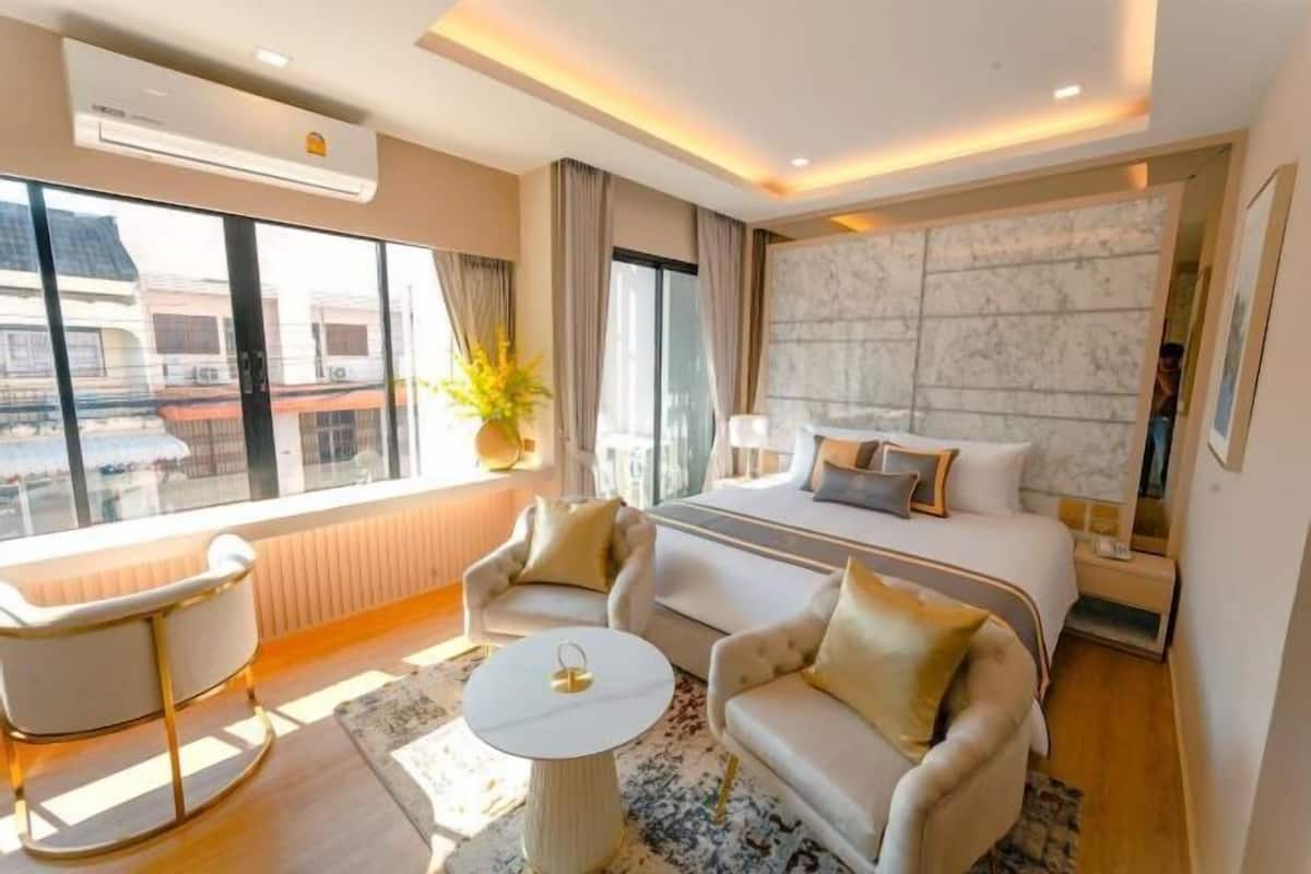 Une chambre d’hôtel moderne dotée d’un grand lit, de deux canapés, d’une table basse ronde et offrant une vue sur les bâtiments grâce à de grandes fenêtres.