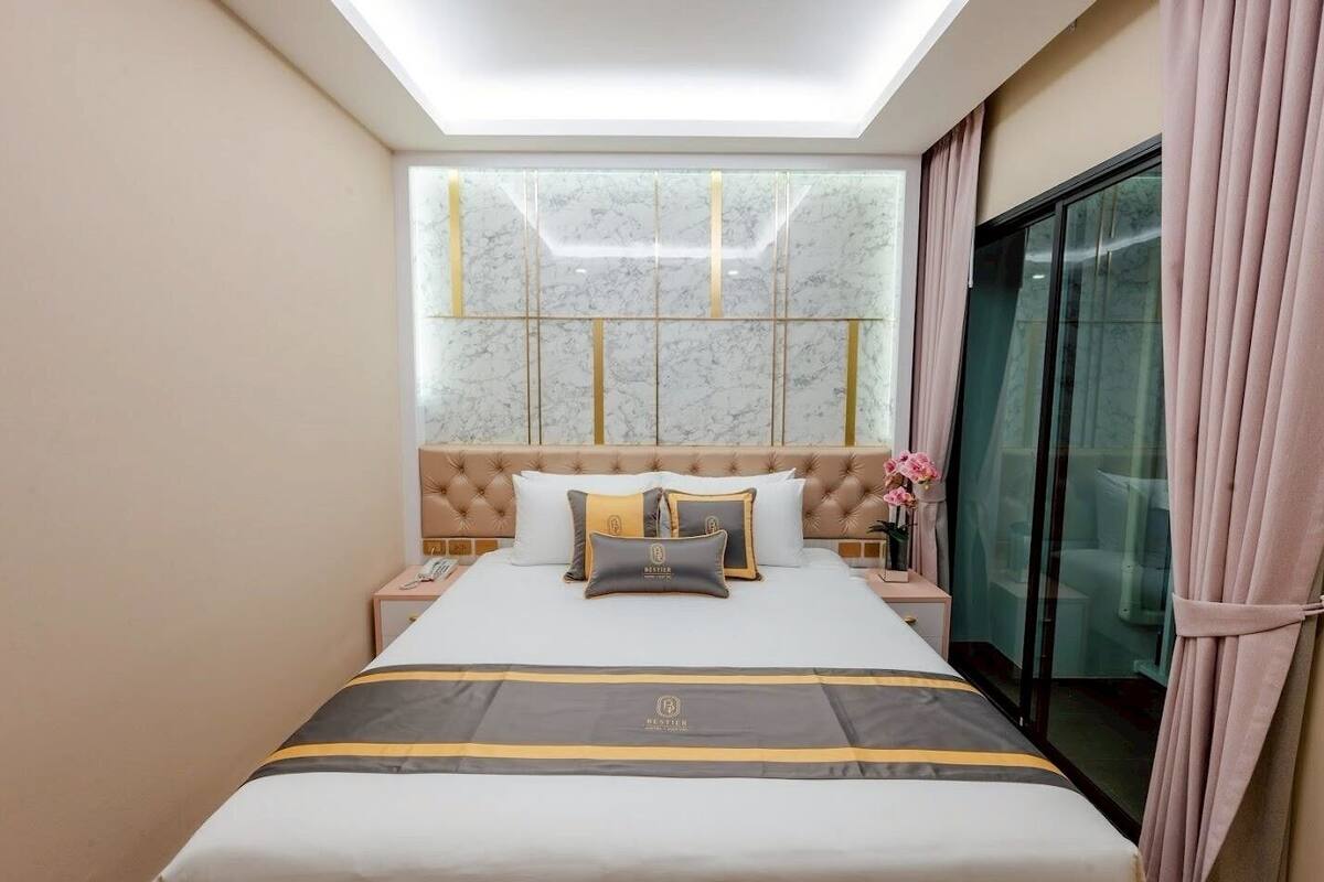 Ein Hotelzimmer mit einem Bett, einem Nachttisch, einem Telefon, einer Blumenvase und einem Vorhangfenster.