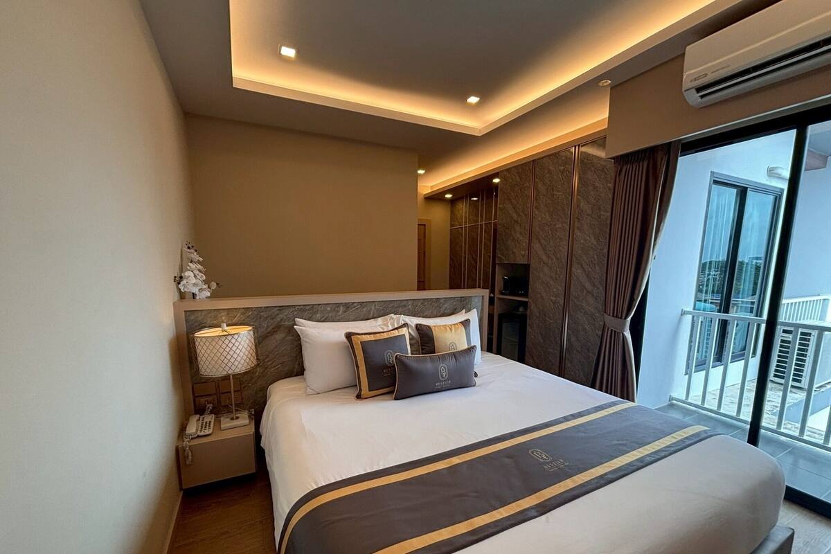 Ein modernes Hotelzimmer mit einem großen Bett, einem Nachttischtelefon, einer Lampe und Blick auf den Balkon.