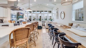 A spacious kitchen with a long island, wicker chairs, and a dining area with a large table. - Classic Coastal Charm w/ Modern Style & Amenities @Cinnamon Shore South! (Port Aransas)