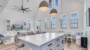 Una cocina amplia con una isla grande, armarios blancos e iluminación colgante.